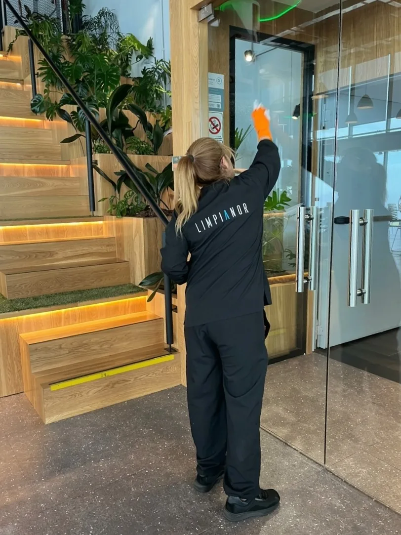 Empleada de Limpianor limpiando un vidrio en el hall de un edificio corporativo